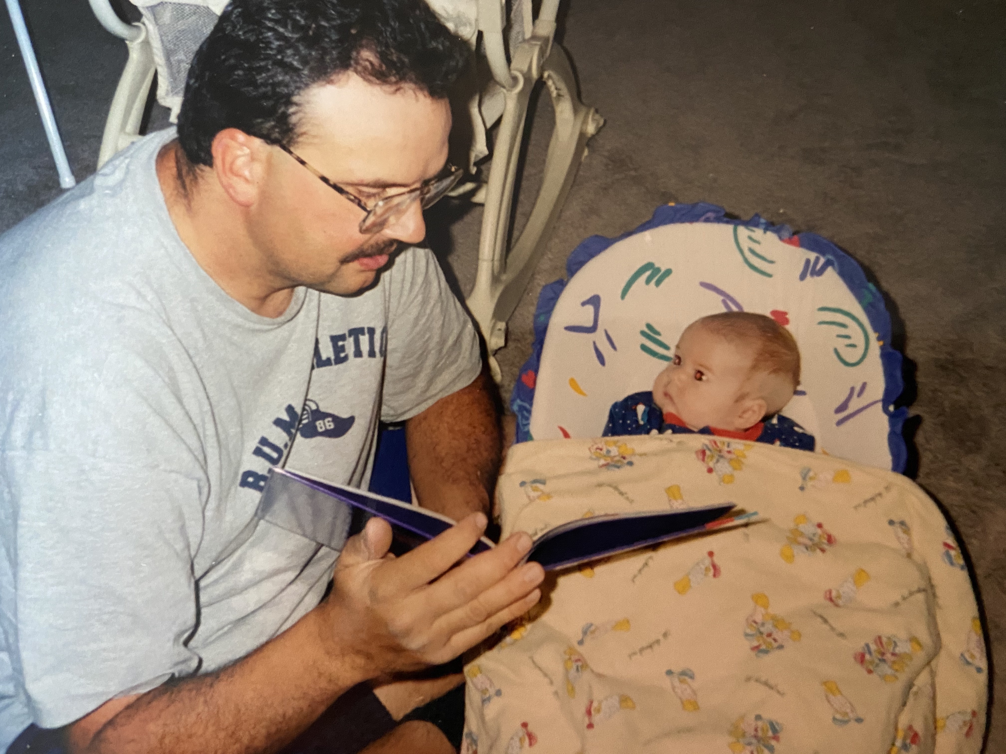 Man holding a book and reading to an infant in a bassinet 